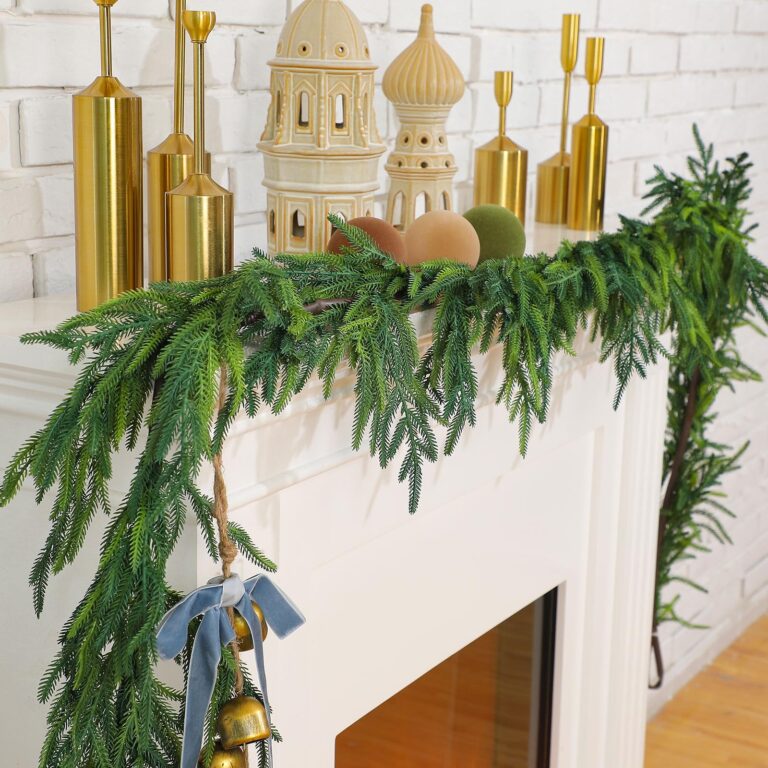 Festive mantel decoration featuring the best Christmas garlands, gold ornaments, and architectural miniatures, all set against a white brick wall.