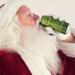 A person in a Santa costume drinks from a green can.
