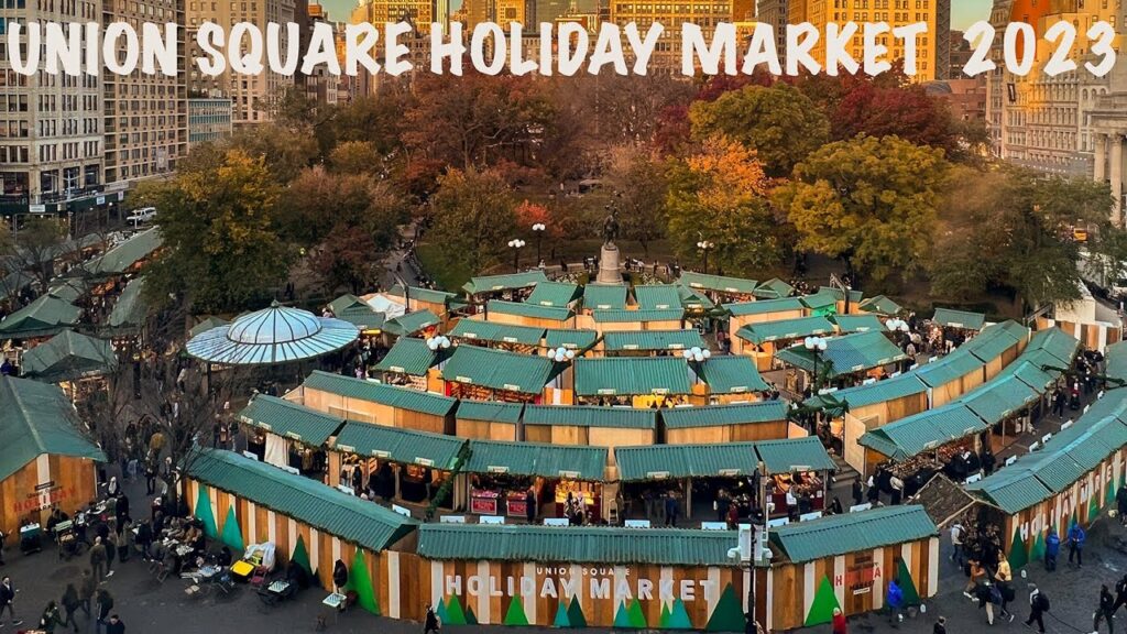 Aerial view of Union Square Holiday Market 2023 with rows of green-roofed vendor stalls, people walking, and trees with autumn leaves in the background.