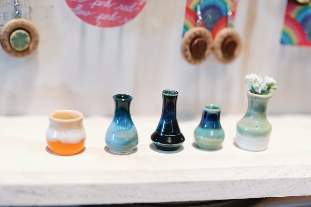 Christmas Markets Massachusetts 2025: Best Festive Events and Holiday Fairs 3 Five small ceramic vases of varying shapes and colors are displayed in a row on a white shelf, with earrings and decorative items blurred in the background.