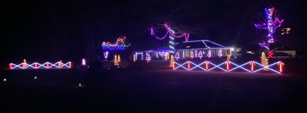 10 Jaw-Dropping Christmas Light Displays in Mississippi You Can’t Miss in 2025! 2 A house and yard are decorated with colorful Christmas lights, including fence outlines, roof trim, trees, and bushes illuminated in purple, blue, red, and white.