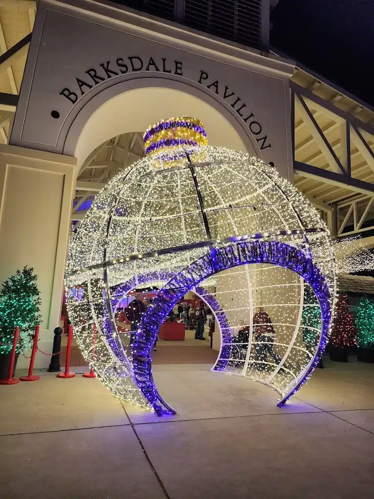 10 Jaw-Dropping Christmas Light Displays in Mississippi You Can’t Miss in 2025! 2 A large, illuminated ornament decoration stands in front of the Barksdale Pavilion entrance, with festive lights and holiday trees nearby at night.