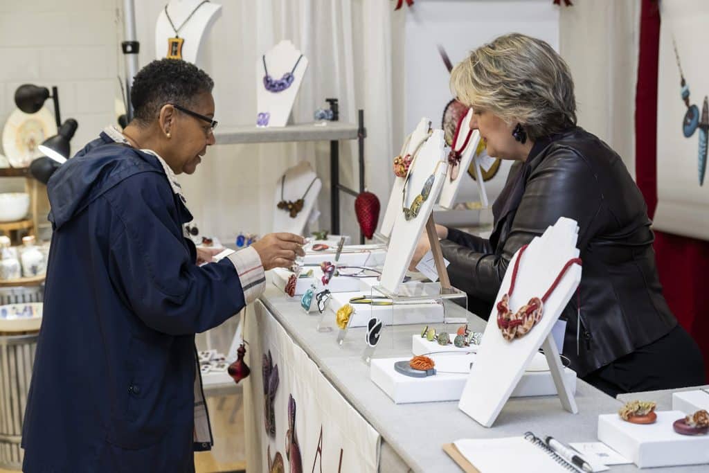 50 Magical Christmas Markets in Virginia for 2025 You Can’t Miss: Ultimate Guide to Festive Events & Holiday Shopping 4 A customer and a vendor interact at a jewelry booth displaying various necklaces and accessories on stands and shelves.