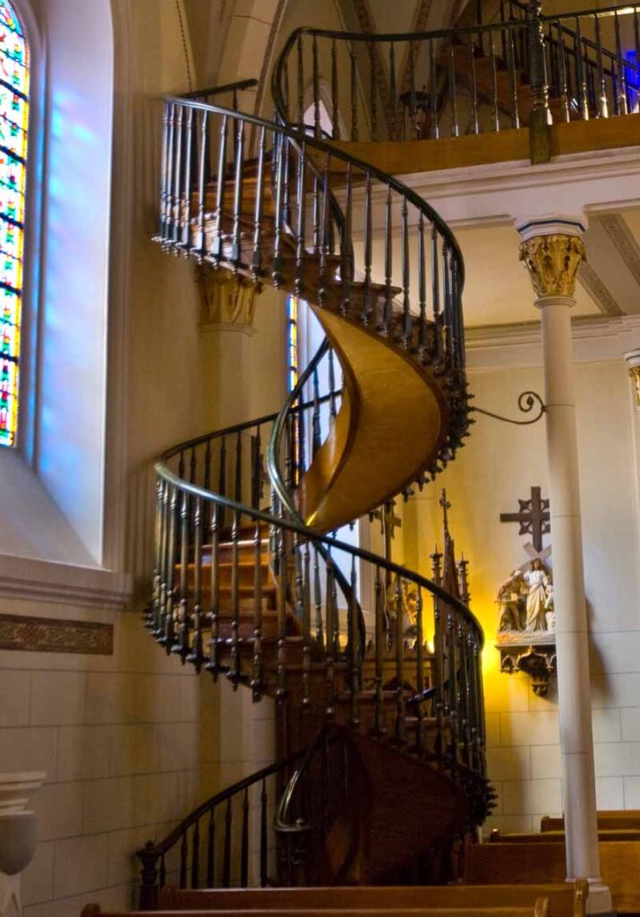 Best Christmas Light Shows New Mexico 2025: Top 7 Festive Displays Across the State 3 A wooden spiral staircase with no central support, surrounded by wrought iron railings, inside a church with stained glass windows and religious statues.