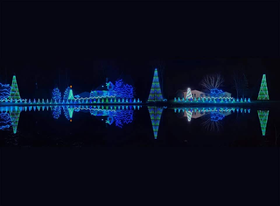 10 Dazzling Christmas Light Shows in Michigan You Can’t Miss in 2025 (Plus Free Spots & Secret Local Favorites!) 8 Houses and trees decorated with blue and green Christmas lights are reflected in a calm body of water at night.