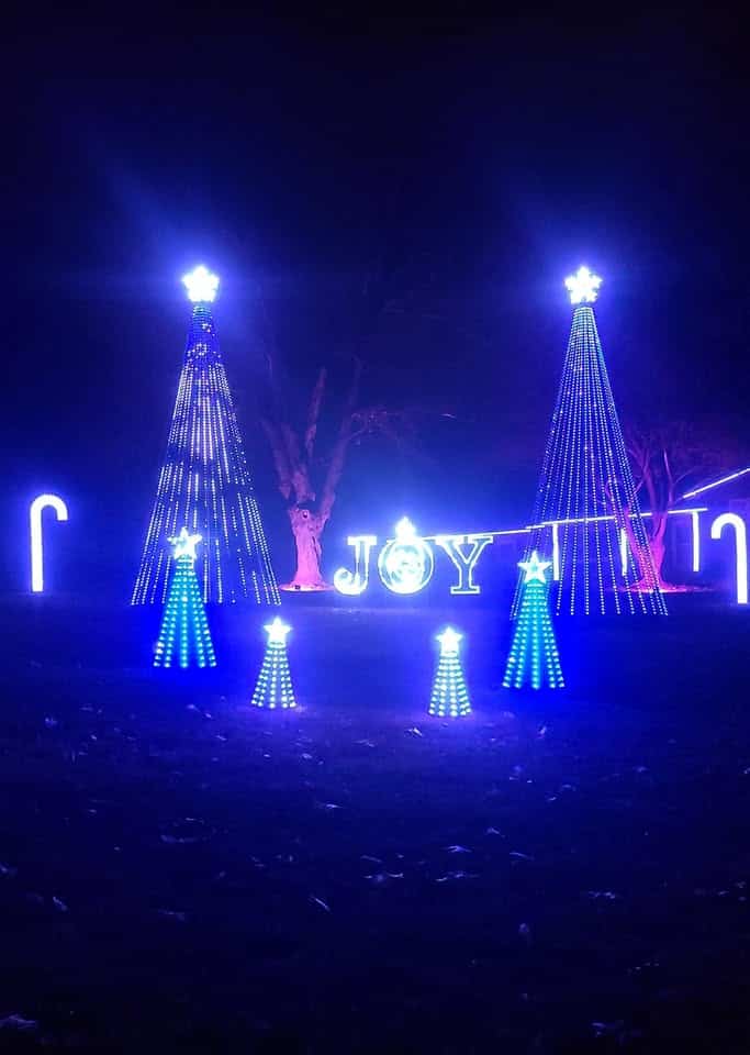 20 Magical Christmas Light Displays in Missouri You Can’t Miss This Holiday Season! (#6 is Jaw-Dropping) 6 Outdoor holiday light display at night featuring blue-lit trees, two candy canes, and the word "JOY" illuminated in white lights.