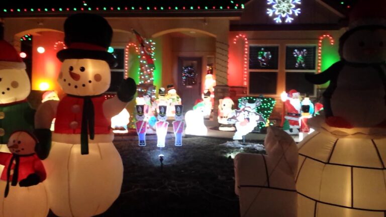 Inflatable snowmen, toy soldiers, and various Christmas decorations, brightly lit with colorful lights, displayed in a yard in front of a house at night.