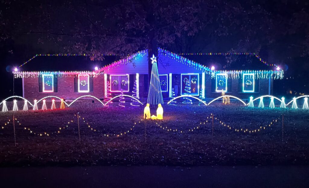 20 Magical Christmas Light Displays in Missouri You Can’t Miss This Holiday Season! (#6 is Jaw-Dropping) 5 A house decorated with colorful Christmas lights, featuring a lit tree, nativity figures on the lawn, and various patterns of string lights along the roof and yard.