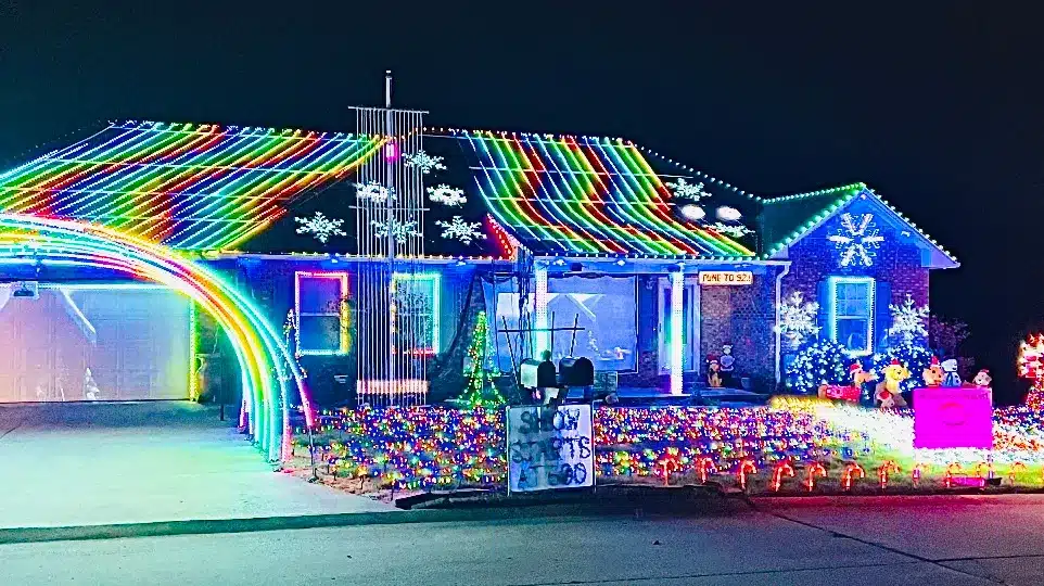 20 Magical Christmas Light Displays in Missouri You Can’t Miss This Holiday Season! (#6 is Jaw-Dropping) 3 A house decorated with colorful Christmas lights, featuring rainbow patterns on the roof and lawn, illuminated snowflakes, and a sign reading "Show starts at 6:30.