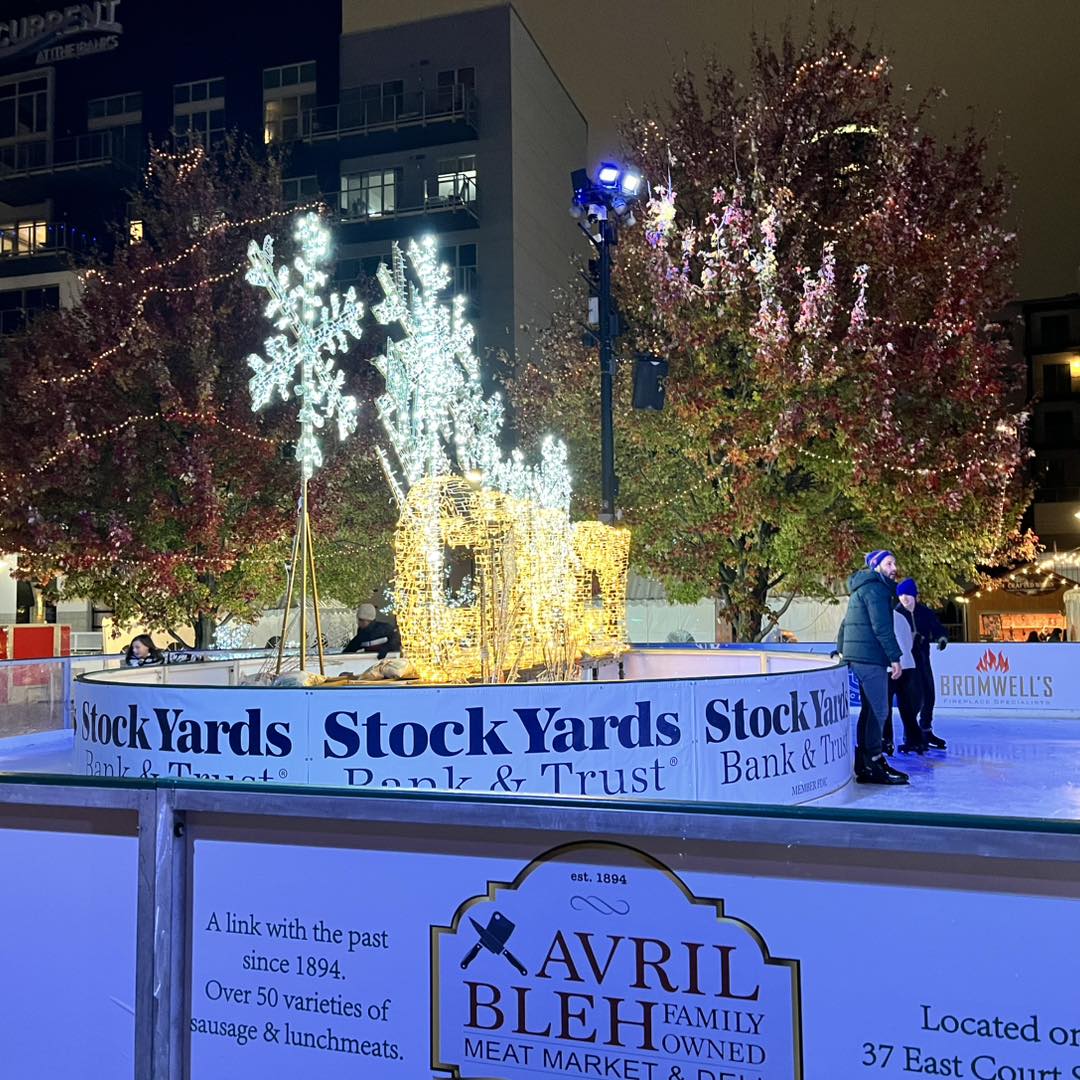 Ohio Christmas Markets 2025: 50 Unforgettable Holiday Events & Festive Fairs You Have to Visit 1 Outdoor ice skating rink with people skating near a decorative, illuminated carriage and snowflakes, surrounded by trees with autumn leaves and business advertisements on the boards.