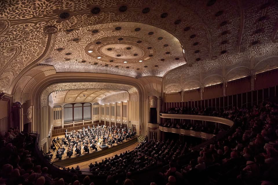 Ohio Christmas Markets 2025: 50 Unforgettable Holiday Events & Festive Fairs You Have to Visit 2 A full orchestra performs on stage in a grand concert hall with ornate ceiling details and an audience seated in balconies and main floor.