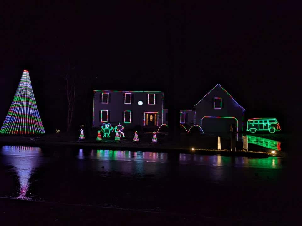10 Jaw-Dropping Christmas Light Shows in New Hampshire You Can’t Miss in 2025 (With Insider Tips & Hidden Gems!) 2 A house and yard are decorated with colorful Christmas lights, including a large tree, figures, and a bus outline, all reflected on a wet surface at night.