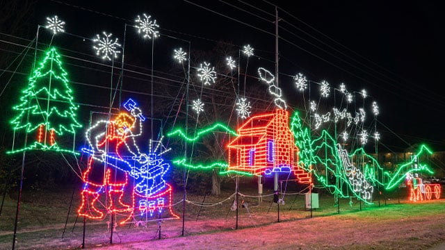 You won't Want To Miss Tennessee’s Most Magical Christmas Markets and Holiday Fairs for 2025 3 Colorful holiday light display depicts a blacksmith, a house, trees, snowflakes, a train, and smoke on a nighttime outdoor scene.