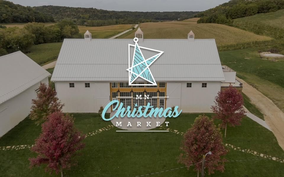 Minnesota’s 50 Best Christmas Markets to Visit in 2025 (You’ll Love #7!) 1 A large white barn with a gray roof is surrounded by trees with red leaves; text overlay reads "MN Christmas Market" with a star graphic above.
