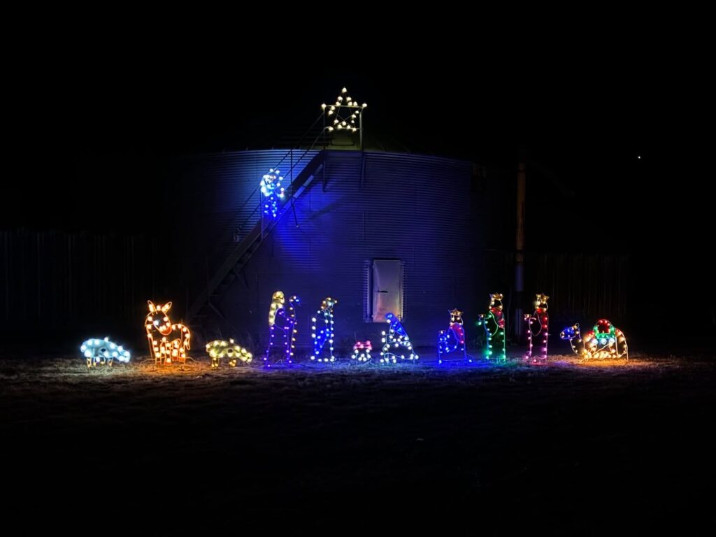 7 Jaw-Dropping Christmas Light Shows in Nebraska You Can’t Miss This Holiday Season (2025 Guide!) 1 A nativity scene made of colorful Christmas lights is displayed in front of a metal grain bin at night, with a lit star and angel above on the bin’s staircase.