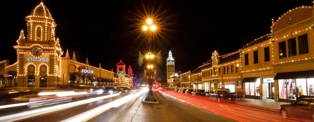 Kansas Christmas Light Shows 2025: The Ultimate Guide to the Most Stunning Holiday Displays You Can’t Miss! 5 Nighttime view of a city street with buildings decorated in holiday lights, light trails from passing cars, and a central tower in the background.