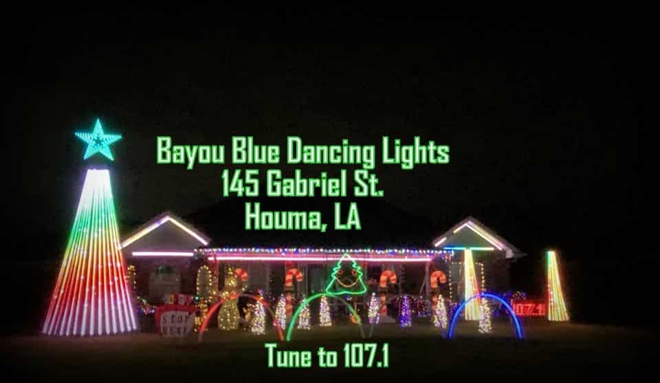 Louisiana’s Ultimate 2025 Christmas Light Displays: Discover The Most Magical, Must-See Holiday Shows You Can’t Miss! 2 House decorated with colorful holiday lights, including a large lit tree and arches, with text reading: "Bayou Blue Dancing Lights, 145 Gabriel St., Houma, LA. Tune to 107.1.