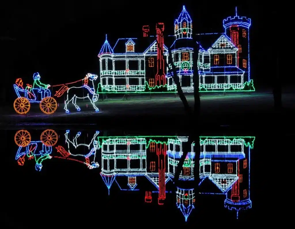 Massachusetts’ Most Magical Christmas Light Displays That Families Can’t Stop Talking About in 2025 4 Holiday lights display of a horse-drawn carriage passing a large castle, with colorful lights reflected in water below at night.