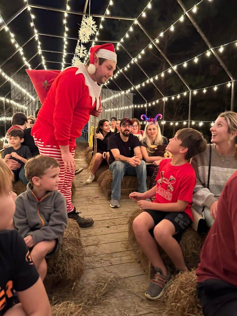 Louisiana’s Ultimate 2025 Christmas Light Displays: Discover The Most Magical, Must-See Holiday Shows You Can’t Miss! 8 A man in a festive elf costume talks to a smiling boy on a hay bale, surrounded by families under a canopy of string lights.