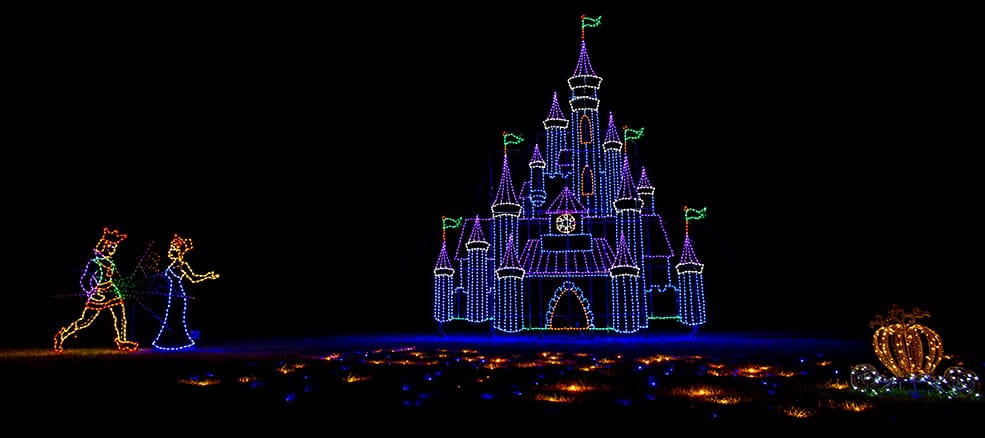 7 Jaw-Dropping Maryland Christmas Light Shows in 2025 You Can’t Afford to Miss! 2 Colorful lights depict a fairy tale castle, a pumpkin carriage, and two figures approaching the castle against a dark background.