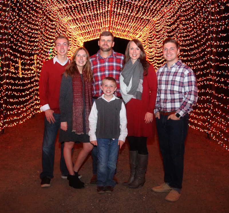 Louisiana’s Ultimate 2025 Christmas Light Displays: Discover The Most Magical, Must-See Holiday Shows You Can’t Miss! 4 A group of six people, including a child, pose for a photo in front of a tunnel decorated with bright red and orange holiday lights.