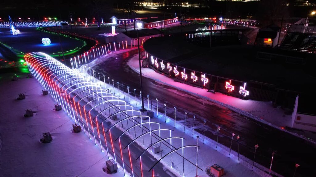 Discover Kentucky’s Jaw-Dropping Christmas Light Spectacles That Will Leave You Breathless This Holiday Season 8 A nighttime view of a drive-through holiday light display with illuminated arches, colorful lights, and decorations set up along a winding path in a snowy area.