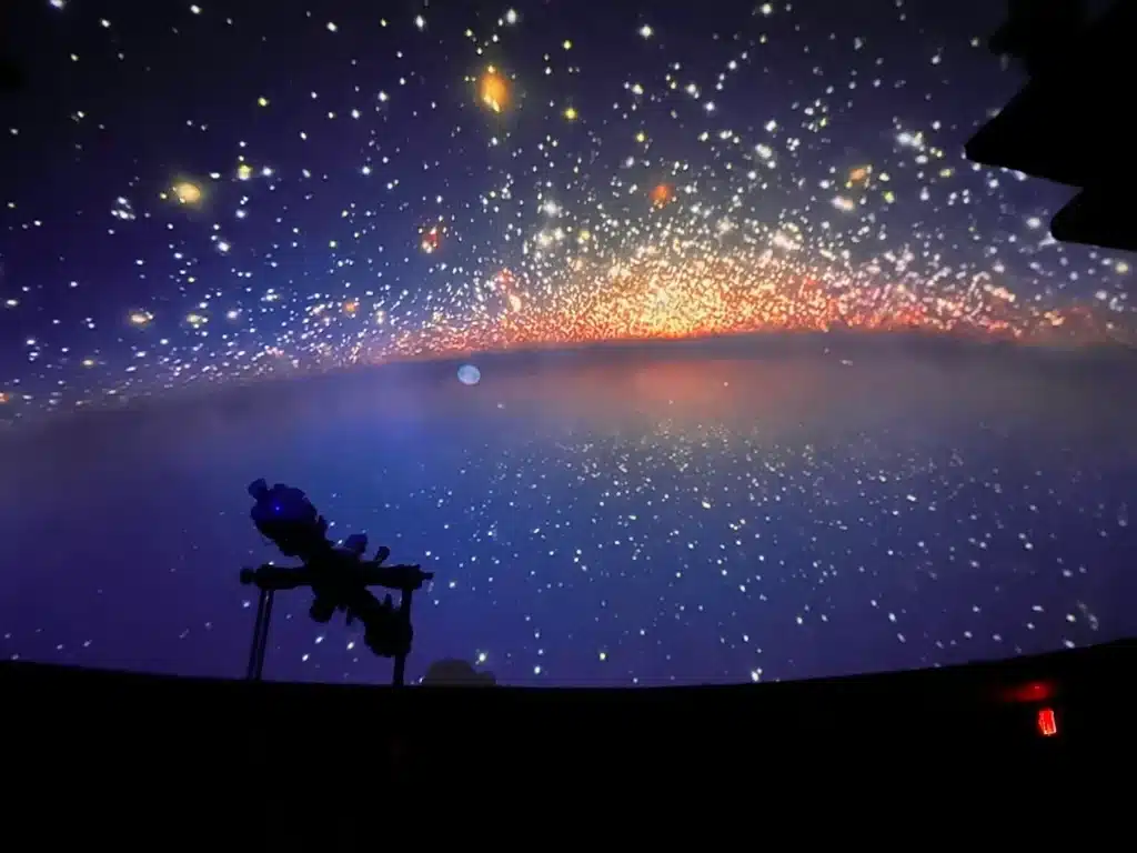 Maine’s Ultimate 2025 Christmas Light Guide: Discover Hidden Sparkling Gems & Holiday Magic Displays You Can’t Miss! 6 A planetarium projection displays a star-filled galaxy scene with a silhouetted telescope in the foreground.