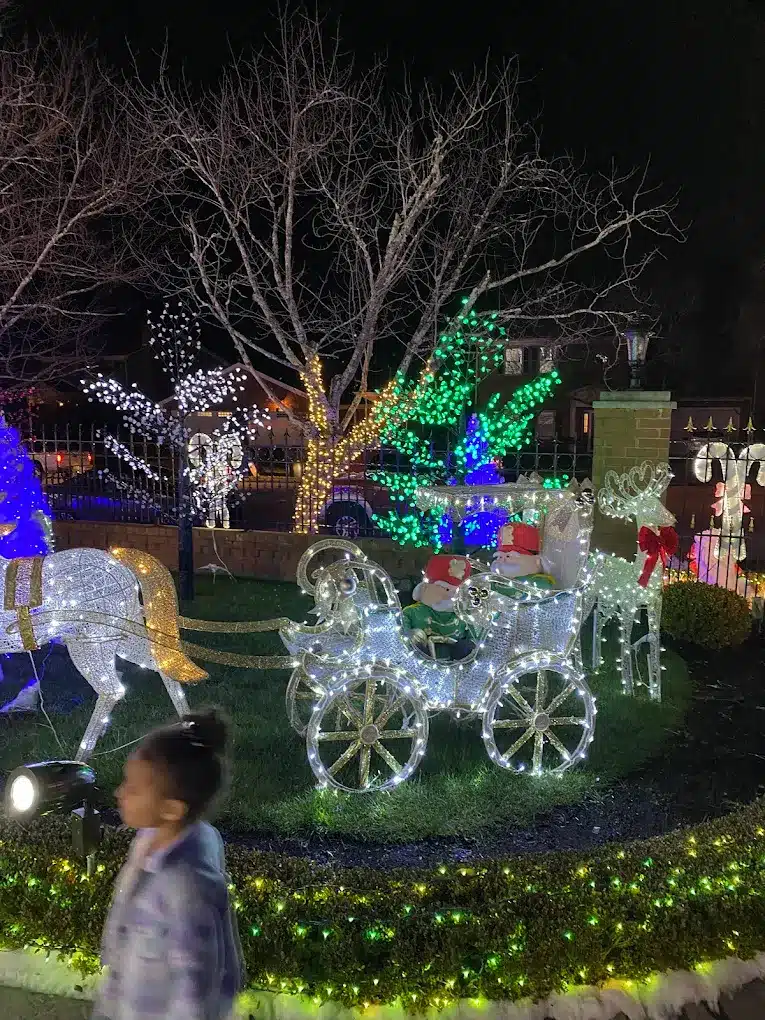 Discover Kentucky’s Jaw-Dropping Christmas Light Spectacles That Will Leave You Breathless This Holiday Season 3 A yard decorated with illuminated Christmas figures, including a horse-drawn carriage, reindeer, and colorful lights, with a child walking in the foreground at night.